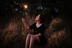 Woman sitting waving a sparkler at night | Honor Credit Union