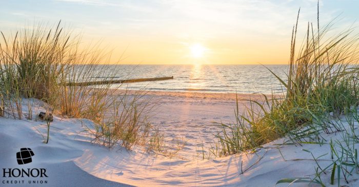 A picture of a sandy beach at sunset with Honor Credit Union's logo in the bottom left corner.