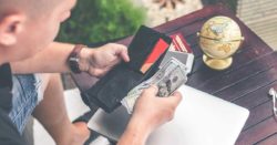 there are several things to know about using honor debit and credit cards abroad; photo of man holding a wallet in front of a table with a laptop and globe on it | Honor Credit Union