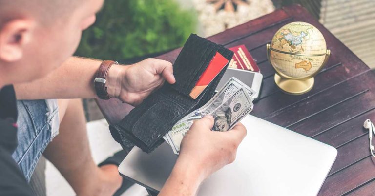 there are several things to know about using honor debit and credit cards abroad; photo of man holding a wallet in front of a table with a laptop and globe on it