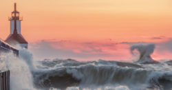 earn up to 2.00 % apy with a surge money market account at honor credit union; waves crashing into a lighthouse at sunset | Honor Credit Union
