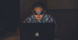 there are practical ways to protect your online identity and profiles; photo of man wearing sunglasses in dark room typing on computer | Honor Credit Union