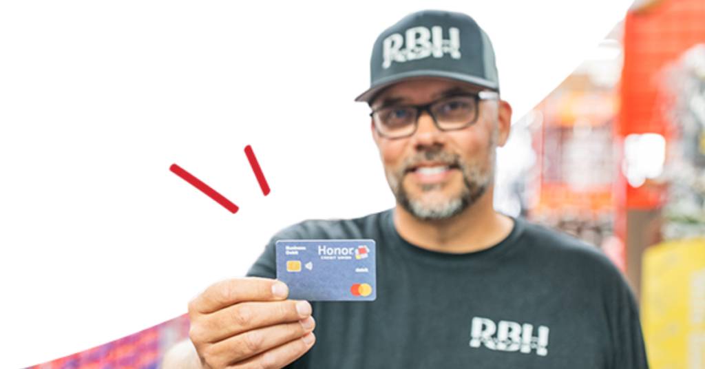 Man in RBH uniform holding a blue Honor Mastercard toward the camera in a store setting. | Honor Credit Union
