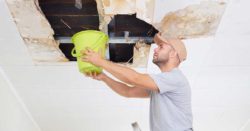 every business should have an emergency fund; photo of man standing on water collecting water falling from the ceiling | Honor Credit Union