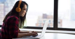 photo of woman sitting at a desk wearing headphones typing on a laptop | Honor Credit Union