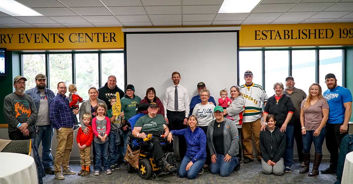 image of northern michigan university hockey coach and players posing for photo with military veterans and other non-profit organization representatives at a check presentation
