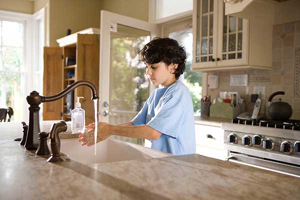 photo of a child washing his hands with soap at a kitchen sink