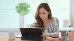 photo of a woman sitting at a table looking at a tablet device