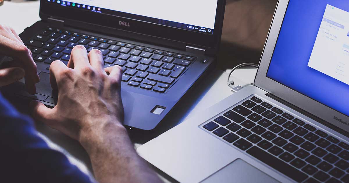 image of a person typing on a dell computer with a Macbook computer next to it