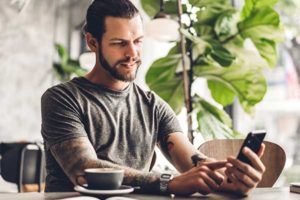photo of a man sitting at a table holding and looking at a smartphone | Honor Credit Union