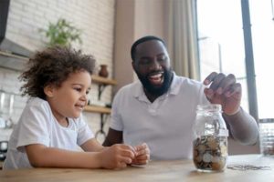 photo of a father and daughter putting loose change in a glass jar at a table | Honor Credit Union
