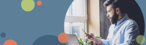 photo of a man looking at a mobile phone while sitting at a desk next to a window | Honor Credit Union