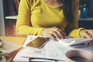 photo of a woman wearing a yellow shirt typing on a calculator while sitting at a table | Honor Credit Union