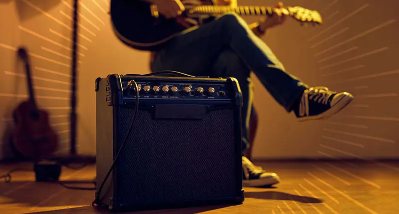 person playing an electric guitar with an amplifier on the ground