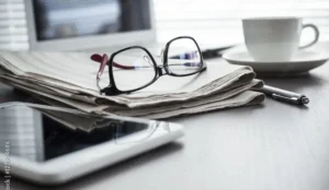 eye glasses on top of a newspaper next to a coffee cup and tablet | Honor Credit Union