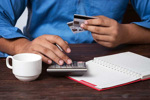 man holding several credit cards while using a calculator