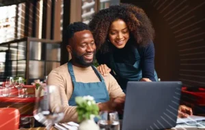 man and woman smiling while looking at a laptop in their business | Honor Credit Union