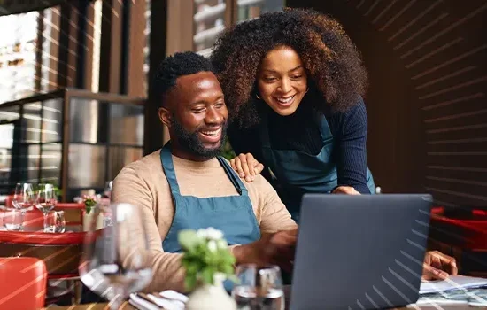 man and woman smiling while looking at a laptop in their business