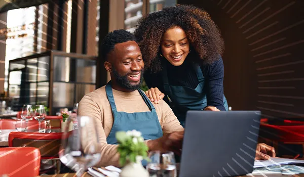 man and woman smiling while looking at a laptop in their business