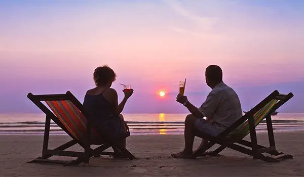 two people sitting on chairs on a beach during sunset