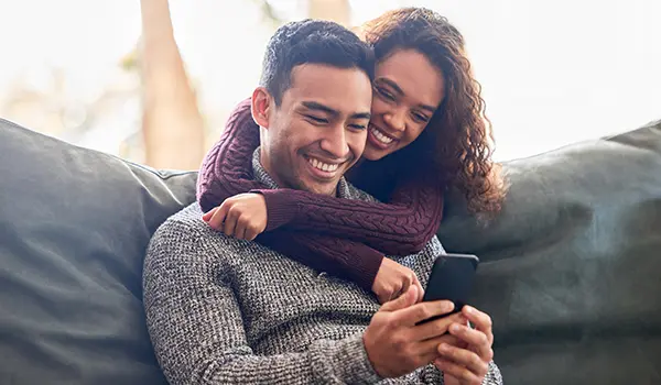 man and woman sitting together looking at a phone and smiling