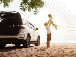 parent lifting child into the air next to an SUV on a beach | Honor Credit Union