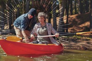 man standing in water helping a woman in a red kayak | Honor Credit Union