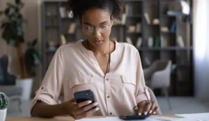 woman sitting at a table looking at a mobile phone | Honor Credit Union
