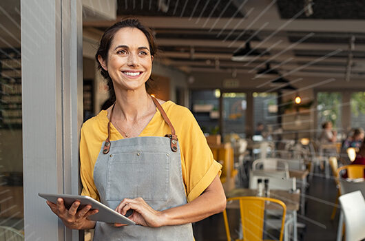 women store owner in an apron holding an ipad