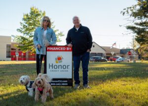 couple standing with an Honor financed by sign with their dogs | Honor Credit Union