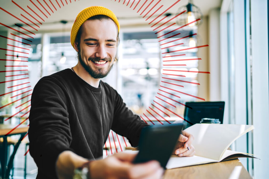 young man holding with a pen and notebook looking at his cell phone smiling