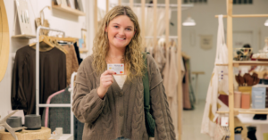 Smiling woman in a cozy knit sweater holding a loyalty card in a clothing boutique. | Honor Credit Union