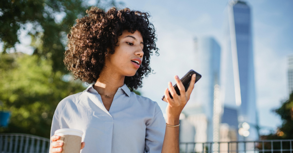 women looking at phone, holding a coffee cup outside | Honor Credit Union