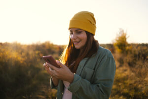 Young hipster female using phone in the field and enjoying sunset. Hiking in nature. | Honor Credit Union