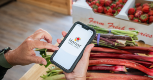 hands holding cell phone with Honor app at market with produce | Honor Credit Union