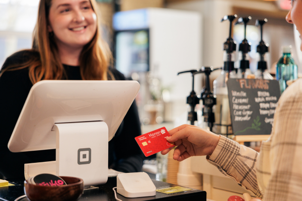 coffee shop clerk at point of sale and women using her Honor Debit card to pay for her order | Honor Credit Union | Honor Credit Union