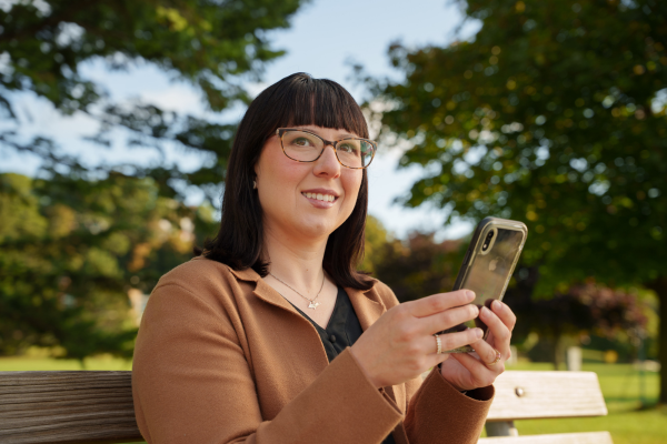 women sitting on a park bench looking at her cell phone | Honor Credit Union | Honor Credit Union