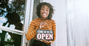 women with an open sign in front of her business | Honor Credit Union