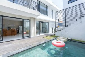 Contemporary white home with large glass doors, a wooden pool deck, and a rectangular pool with inflatable rings. | Honor Credit Union