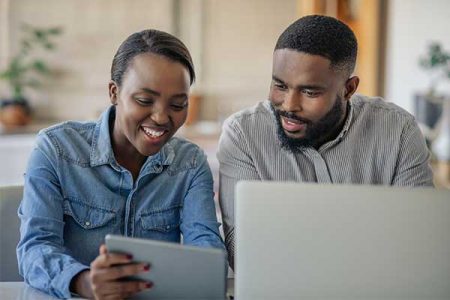 refinance-student-loans man and woman sitting next to each other smiling and looking at a tablet device